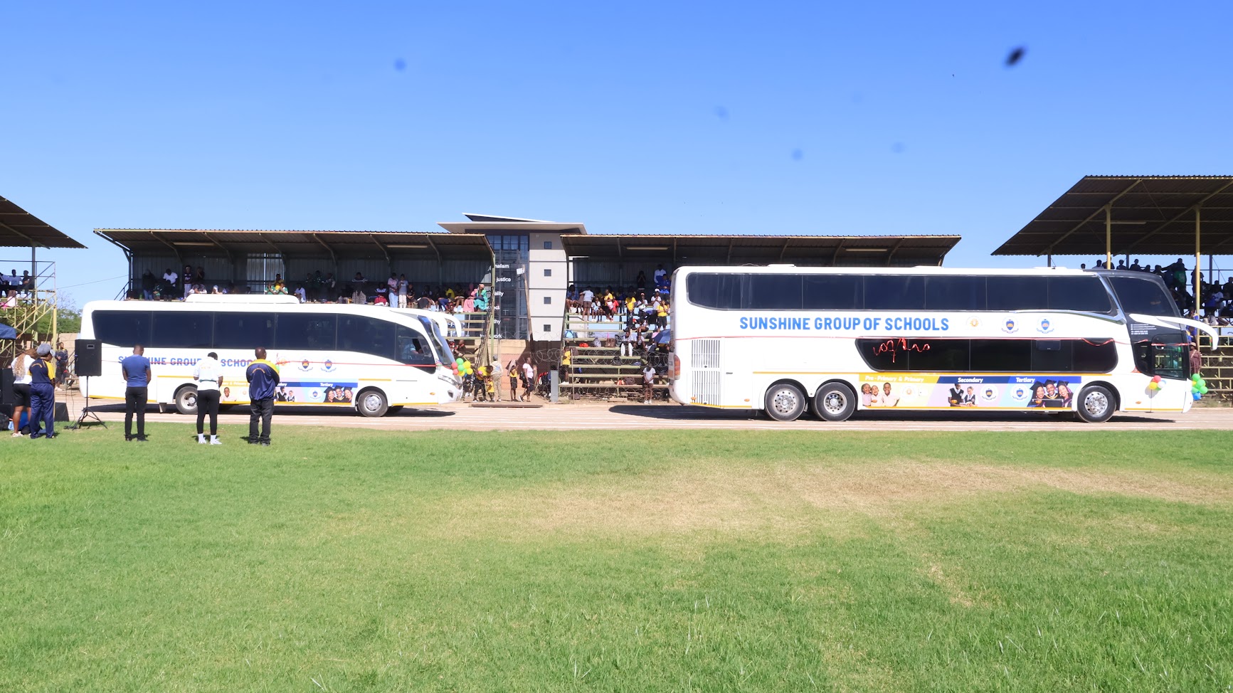 Two Sunshine Group of Schools buses parked beside a sports field